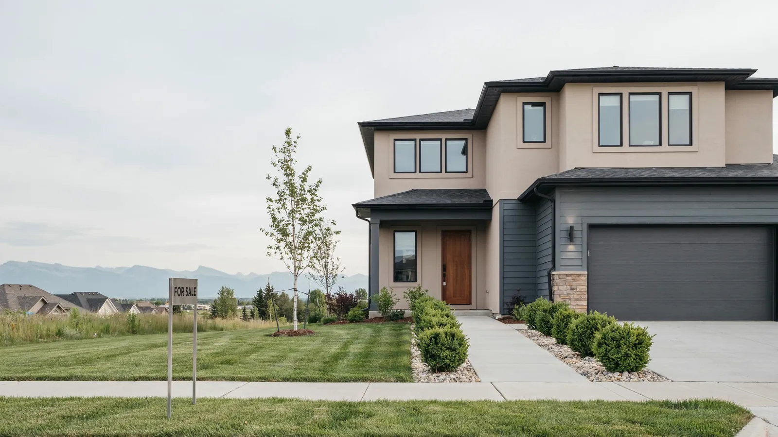 A modern two storey home with mountains behind it and a for sale sign on the lawn, the Airdrie foreclosure guide